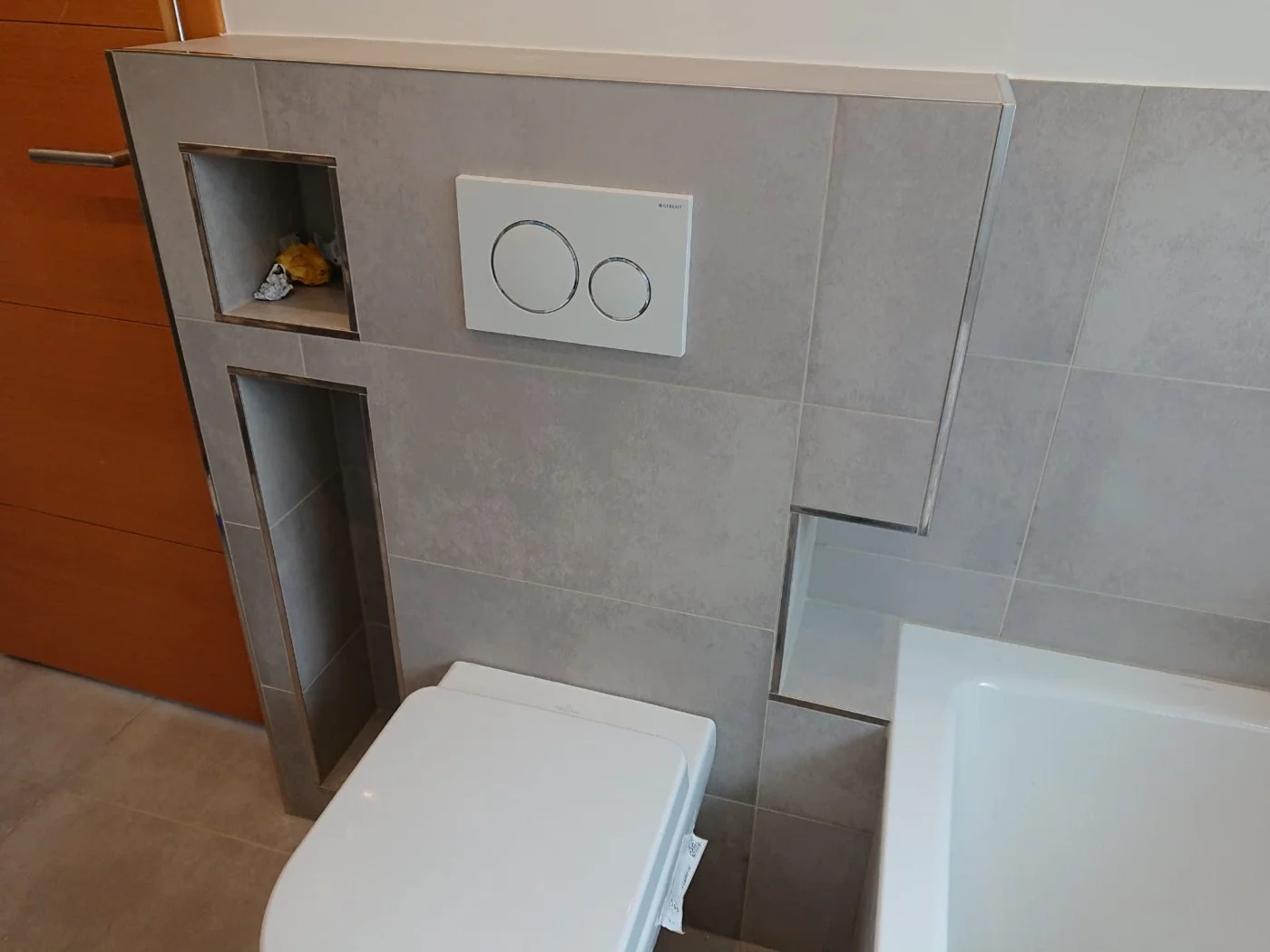 Badezimmer mit praktischen Wandnischen, grauen Fliesen und modernem Toilettenelement