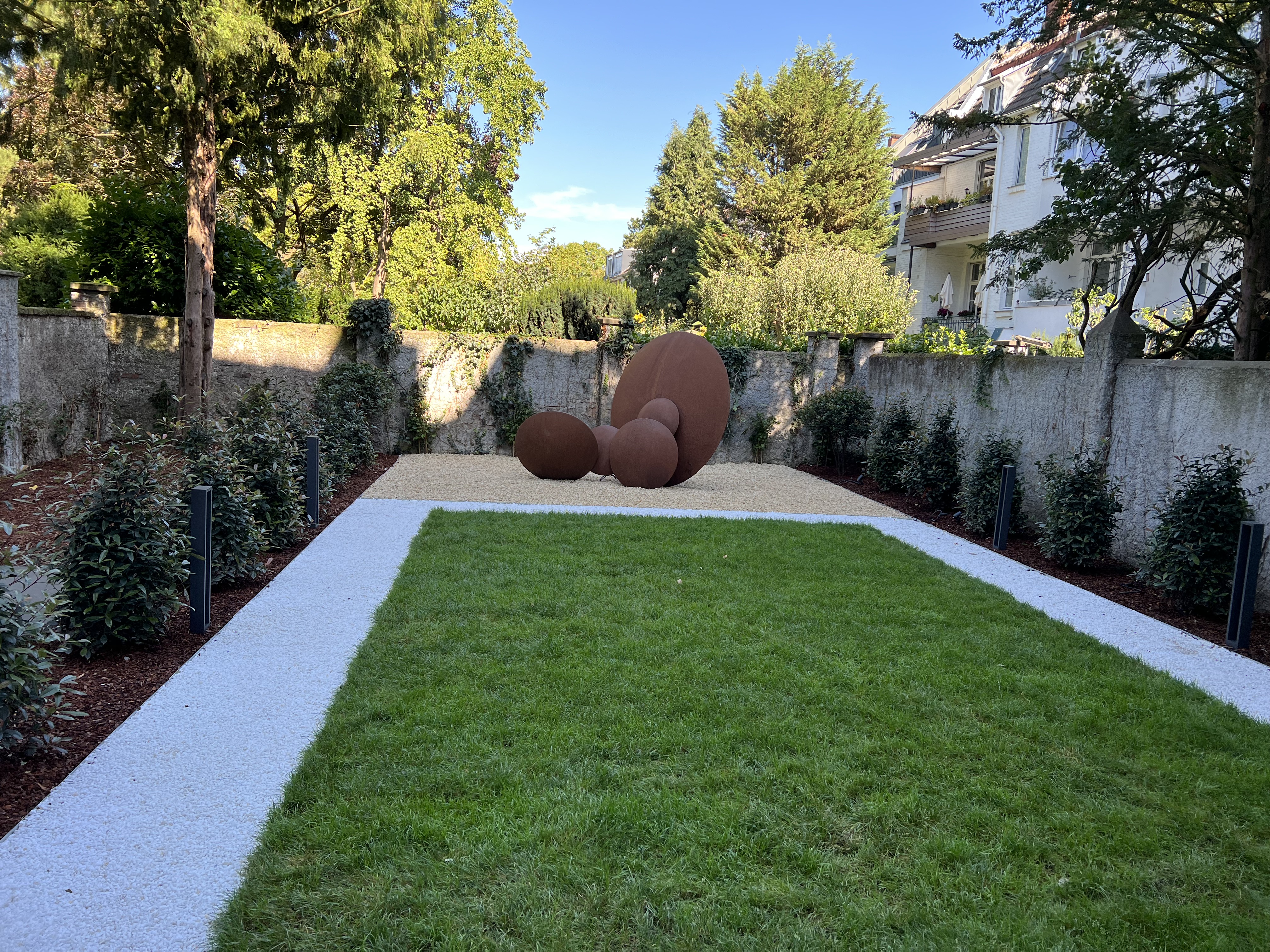 Gestalteter Garten mit Cortenstahl-Kugelskulpturen, Kieswegen und symmetrischer Bepflanzung